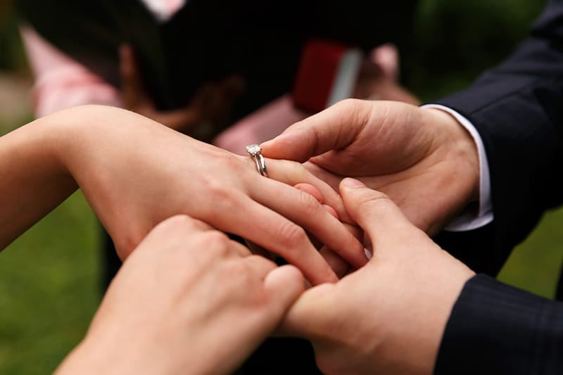 Celebrant Services | Man's hands holding female's hands while touching the ring on her finger.